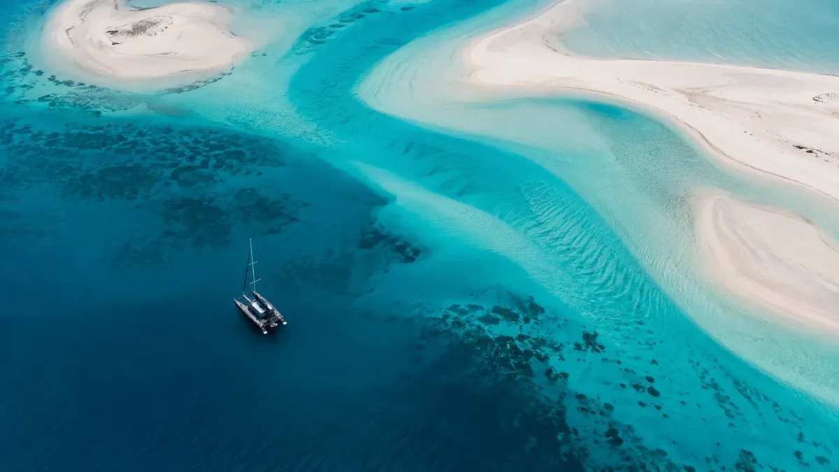Overhead view of a dark catamaran beside sweeping Bahamian-style sandbanks