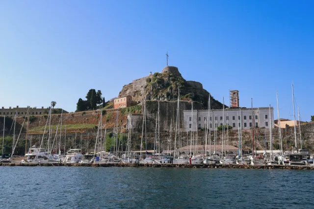 Sailboats and yachts docked in a Mediterranean marina below a hilltop fortress